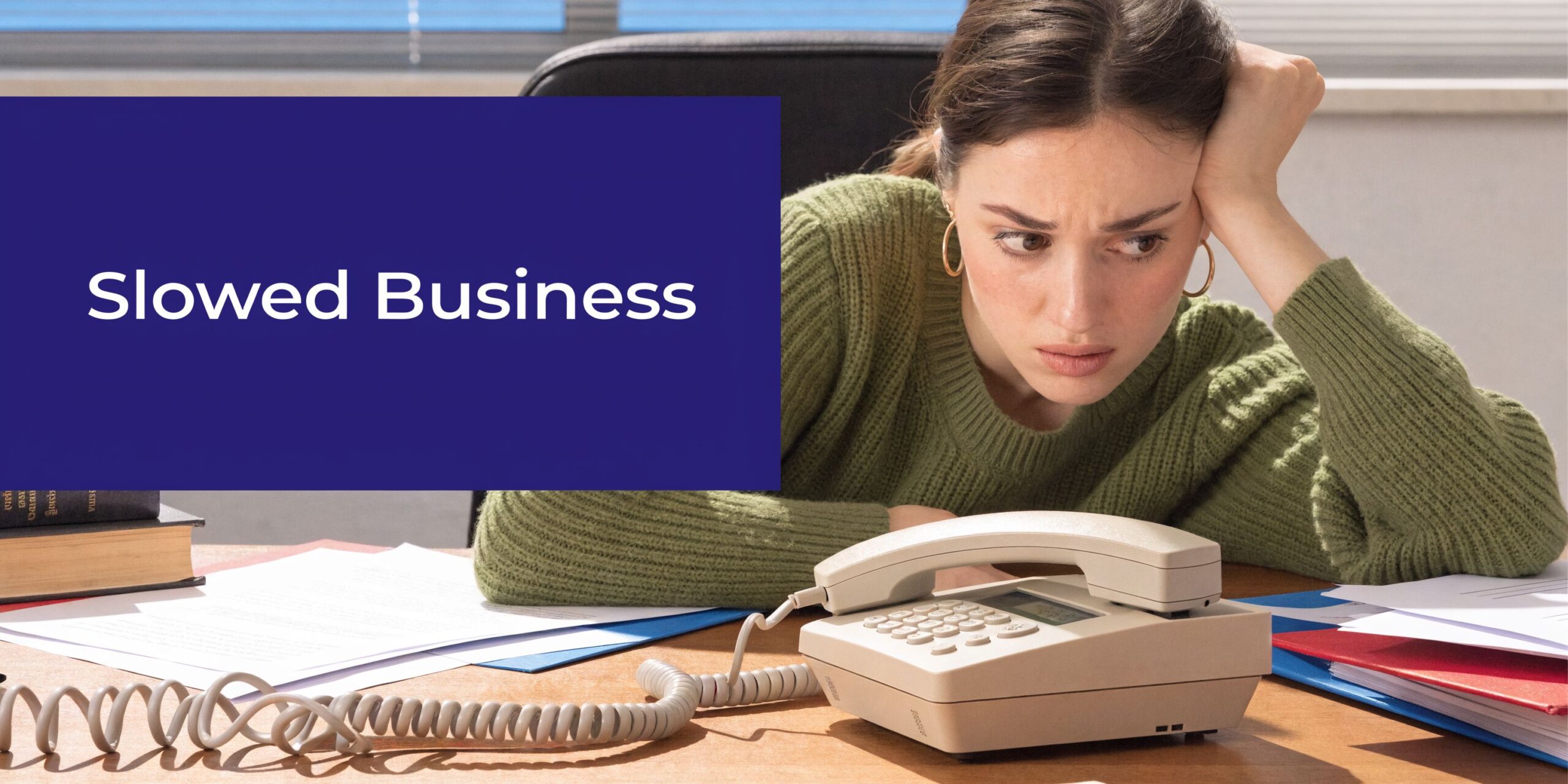 A concerned woman sitting at her desk, waiting for a call on a landline office phone.
