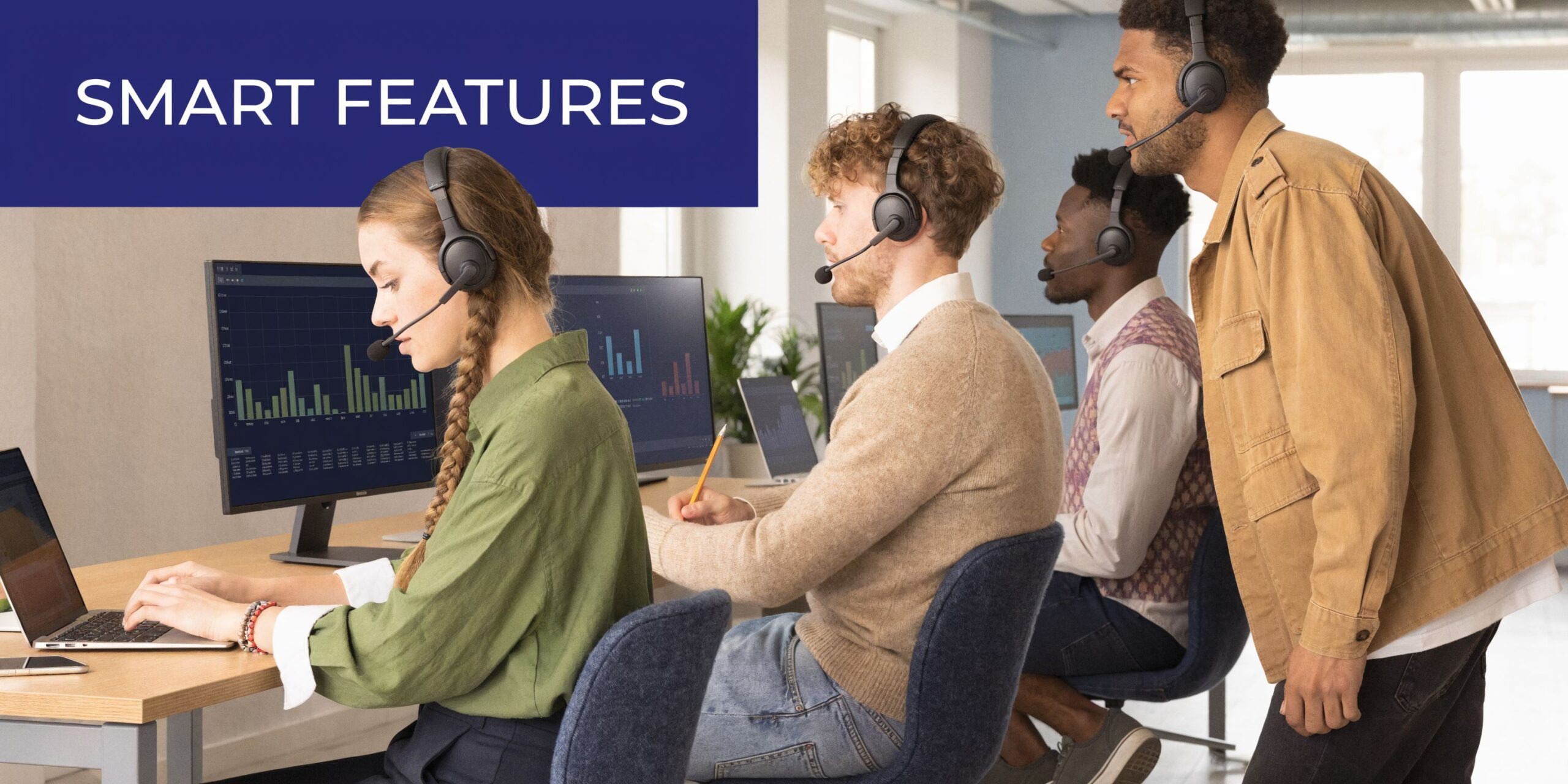 A professional office team wearing headsets working together at desks with computers and data displays.