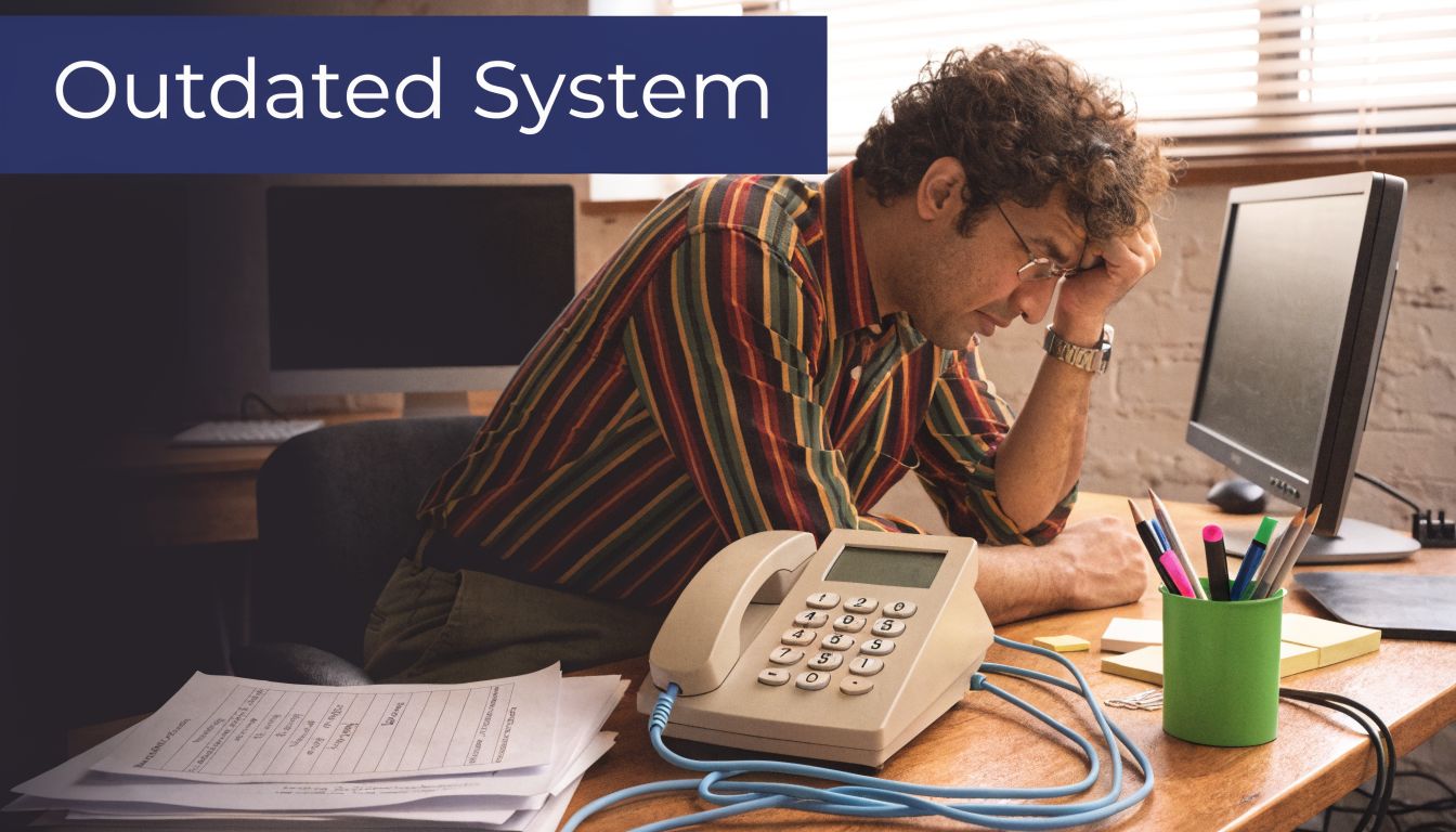 A frustrated office worker sitting at his desk feeling stressed while looking at an outdated telephone system.