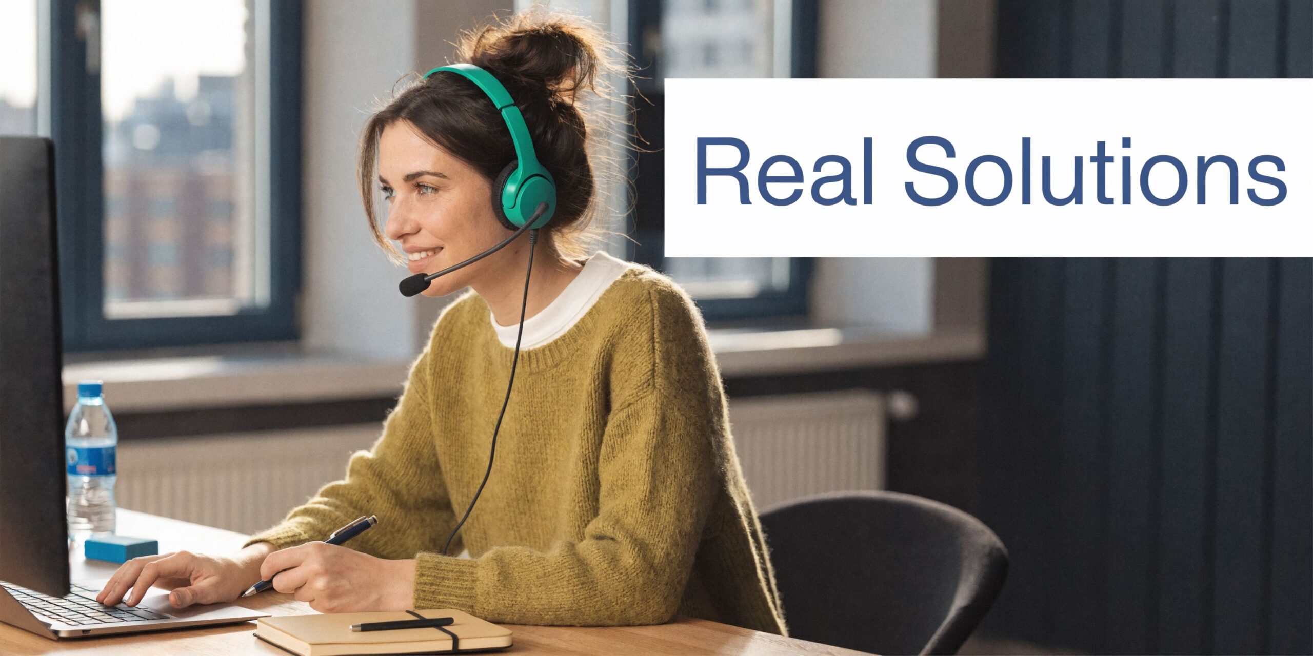 A smiling woman with headphones works at her desk using a computer for business communication.