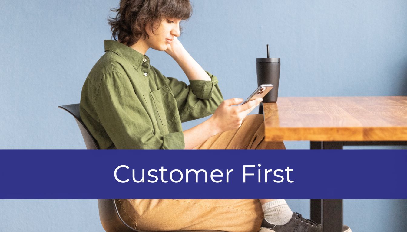 A young person with short hair sitting at a wooden table looking at their smartphone.