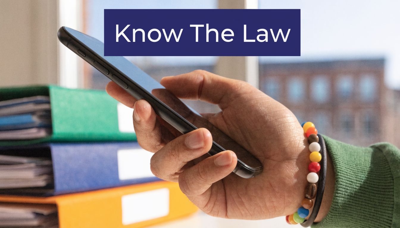 A close-up view of a person's hand holding a smartphone with a legal binder stack background.