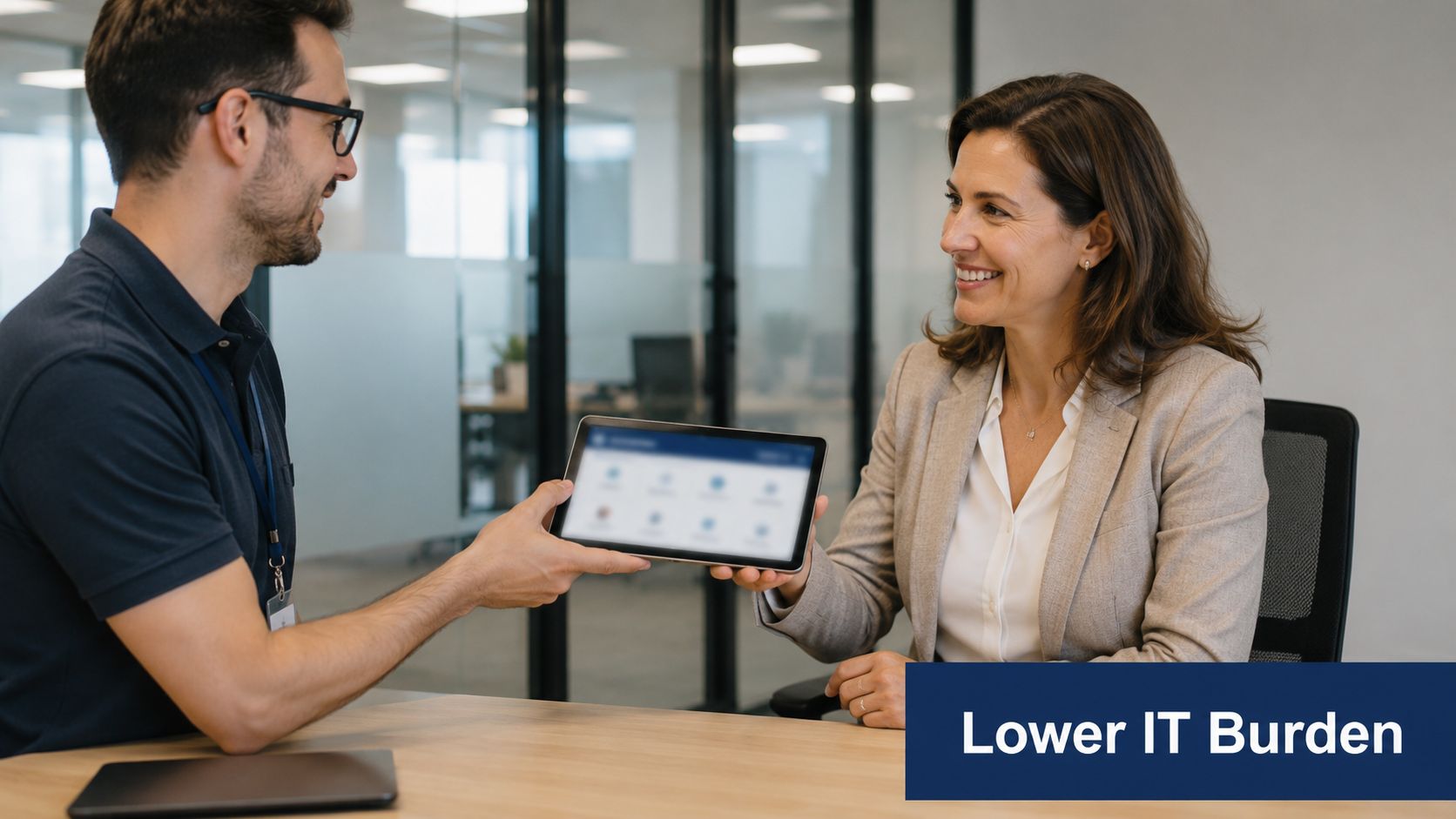 A professional man and woman discussing business while looking at a tablet in a modern office.