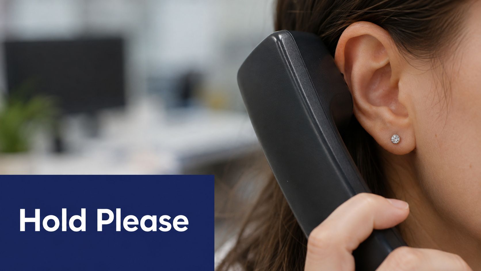 A close-up view of a person holding a telephone receiver to their ear in an office.